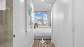 Ein modernes Hotelzimmer mit großem Fenster und Blick auf die Stadt, einer Duschkabine aus Glas und einem ordentlich bezogenen Bett.