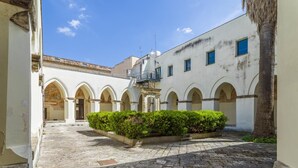 Un patio con jardín central, paseos con arcos y un edificio con balcón.