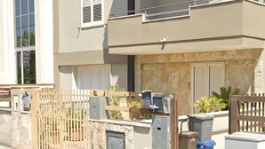 Un edificio residencial con entrada protegida por un portón, fachada de piedra y un pequeño jardín.