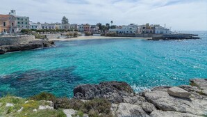 Un pueblo costero con edificios a lo largo del frente marítimo, agua turquesa cristalina y afloramientos rocosos.