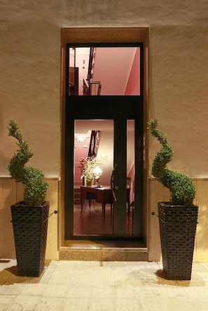 Una puerta flanqueada por dos macetas con plantas, que da paso a un espacio interior con una mesa y sillas.