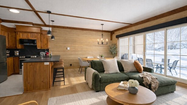 Eine moderne Küche mit Holzschränken, einer zentralen Kochinsel und einem Essbereich mit einem grünen Sofa und einem Couchtisch.