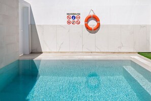 Ein Schwimmbecken mit klarem Wasser, einem Rettungsring und Sicherheitshinweisen an der Wand.