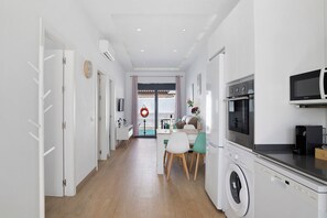 A modern kitchen with a washing machine, a microwave, and a dining area with chairs and a table. - Holiday Home Casas Las Arenas 2 with Private Saltwater Pool, Wi-Fi, and Air Conditioning (Cádiz)