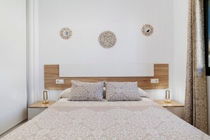 Ein ordentlich eingerichtetes Schlafzimmer mit einem großen Bett, zwei Nachttischen mit Lampen und dekorativen Wandspiegeln.