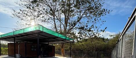 Un espacio al aire libre cubierto con piso de grava, un edificio de madera y un árbol grande.