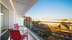 Een balkon met rode rieten stoelen en een kleine tafel, met uitzicht op een stadsgezicht met gebouwen en een drukke weg met bussen.