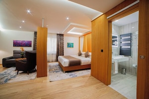 A modern hotel room with a bed, a sofa, a desk, and a bathroom.