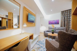 A modern living room with a wooden desk, grey sofa, and a flat-screen TV mounted on the wall.