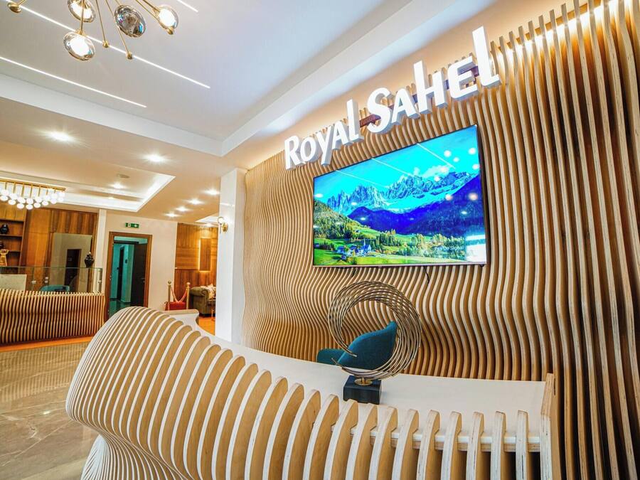 Uma área de recepção com uma televisão grande exibindo uma paisagem cênica, um balcão de atendimento e um design de parede moderno com listras.