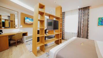 A modern hotel room with a wooden desk, a television, a bed, and a large window with curtains.