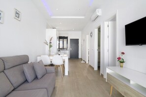 Ein modernes Wohnzimmer mit einer Couch, einem an der Wand befestigten Fernseher und einem Essbereich mit Stühlen und einem Tisch.