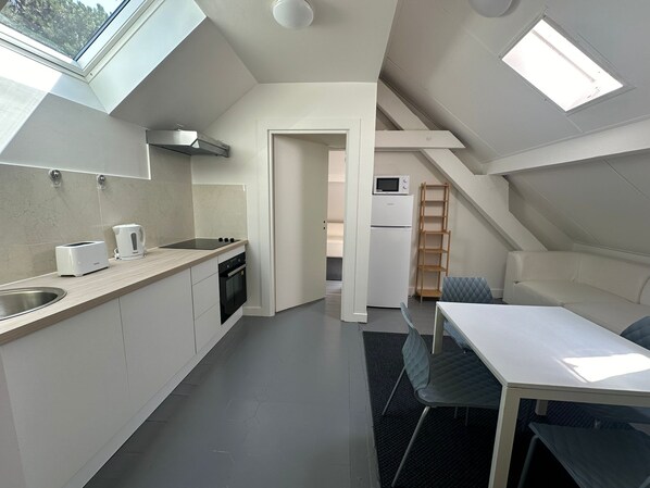 A compact kitchen with a toaster, kettle, and oven, a dining area with a table and chairs, and a small refrigerator.
