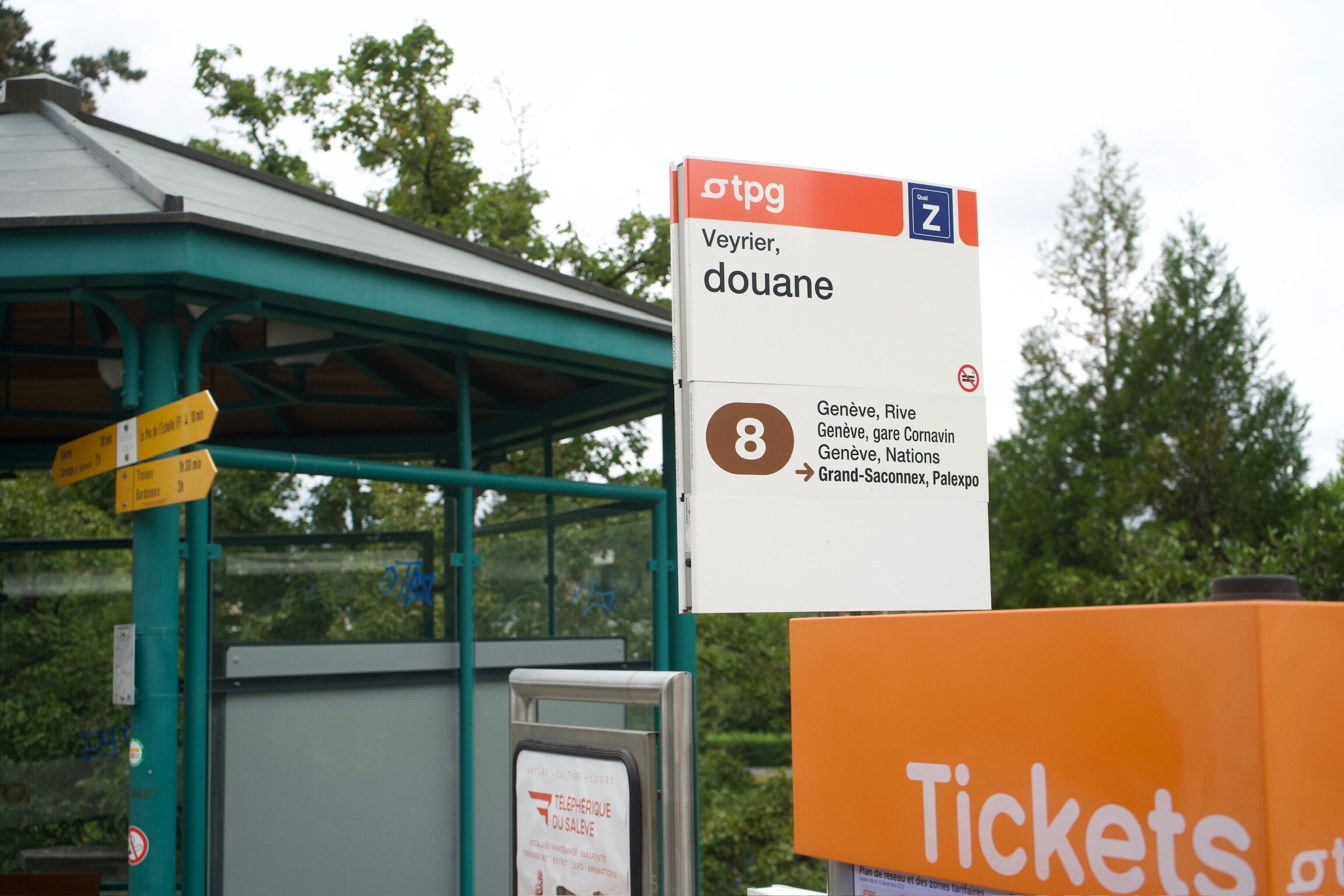 Een bushalte onderdak met een bord waarop 'Veyrier, douane' staat en het lijnnummer '8'.