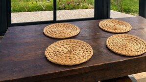Een eettafel met vier gevlochten placemats en uitzicht op een gazon door grote schuifdeuren.
