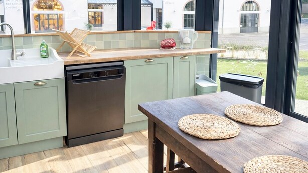 Een moderne keuken met een groot raam, een houten tafel en groene kastjes.