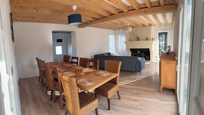 Een eethoek met een houten tafel en rieten stoelen, een bank, en een open haard op de achtergrond.