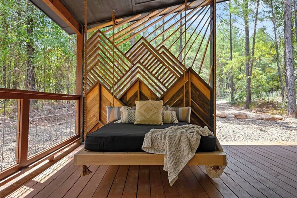 Ein hölzernes Bett mit einem geometrisch gemusterten Kopfteil, einer schwarzen Matratze und mehreren Kissen.