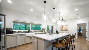 A modern kitchen with a large island, bar stools, and pendant lighting. - StayHocha Luxury Pet Friendly Cabin (Broken Bow)
