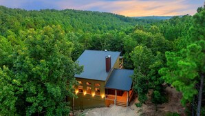 A cabin with a metal roof, surrounded by dense forest. - StayHocha Luxury Pet Friendly Cabin (Broken Bow)