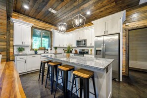 A modern kitchen with white cabinets, a large island with bar stools, stainless steel appliances, and a wooden ceiling. - Luxurious 4 Bedroom Cabin Retreat in Broken Bow (Broken Bow)