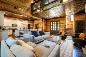 Ein geräumiges Wohnzimmer mit hoher Decke, Holzwänden und einer Küche im Hintergrund.