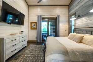 Ein Schlafzimmer mit Bett, Kommode, Fernseher und Blick ins Freie.
