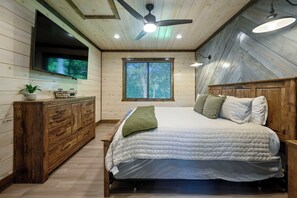 Een slaapkamer met een bed, een houten dressoir, een plafondventilator en een raam met jaloezieën.