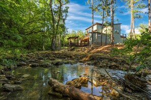 A modern house with a deck overlooking a forested area and a stream. - Creekfront,Pickleball,Game Room,Firepit,Sleeps 16 (Broken Bow)