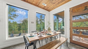 Comedor con mesa de madera dispuesta para seis personas, ventanas amplias y vistas al exterior.