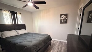 A bedroom with a bed, a ceiling fan, a dresser, and a framed picture on the wall. - Executive Comfort Suite (Weslaco)