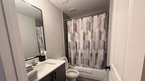 A modern bathroom with a vanity, toilet, and shower curtain. - Executive Comfort Suite (Weslaco)