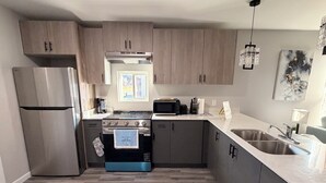 A modern kitchen with stainless steel appliances, wooden cabinets, and a large window. - Executive Comfort Suite (Weslaco)