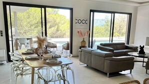 Un salón moderno con comedor, ventanas amplias y vista a una piscina.