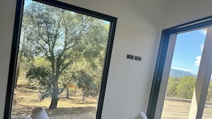 Habitación con una ventana grande que ofrece vistas a árboles y un balcón. Hay dos toallas enrolladas sobre un felpudo beige en la cama.