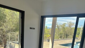 Un dormitorio con una cama grande, vistas a una piscina y un balcón con árboles.