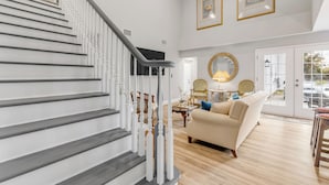 A spacious living area with a staircase, a sofa, a coffee table, and a large mirror. - 5BR Estate • Hot Tub & Sleeps 10 • Near Beach (Edgewater)