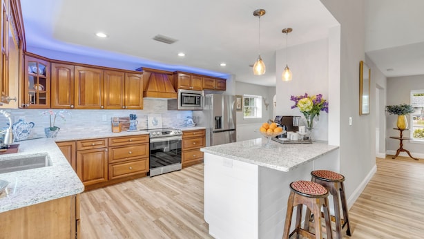 A modern kitchen with wooden cabinets, stainless steel appliances, and a central island with stools. - 5BR Estate • Hot Tub & Sleeps 10 • Near Beach (Edgewater)