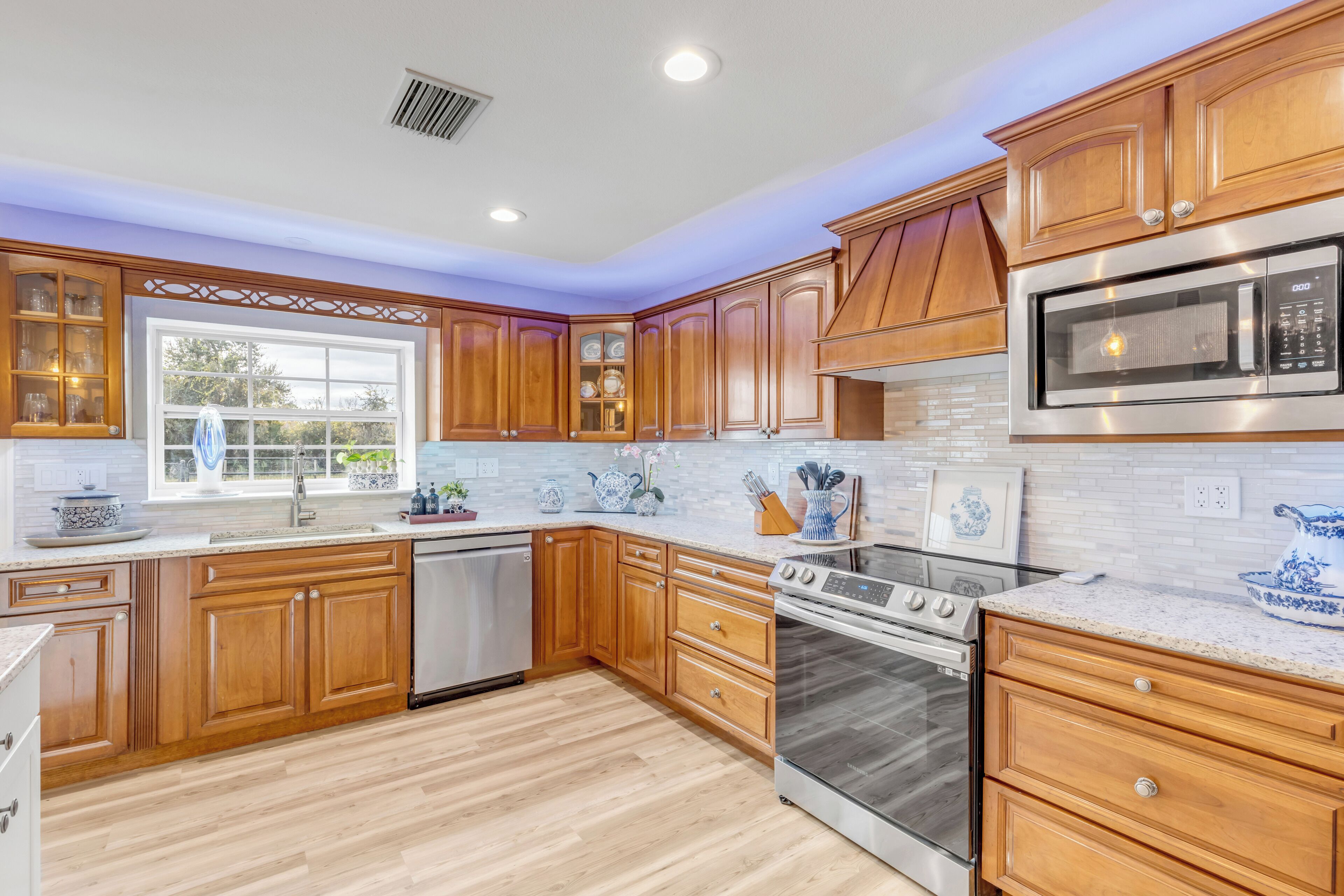 A modern kitchen with wooden cabinets, stainless steel appliances, and a large window.