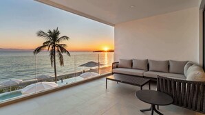 A balcony with a sofa, a table, and a view of the sunset over the sea. - Panarea 1B | Beachfront 3BR + Direct Ocean Views, Sleeps 6 & Resort Pools (Bucerías)