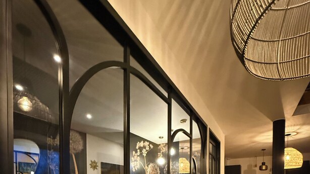 A modern interior with a wooden bar, glass walls, and a dining area. - Ecrin de charme (Granville)