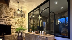 A modern living room with a stone wall, a large window, and a sofa. - Ecrin de charme (Granville)