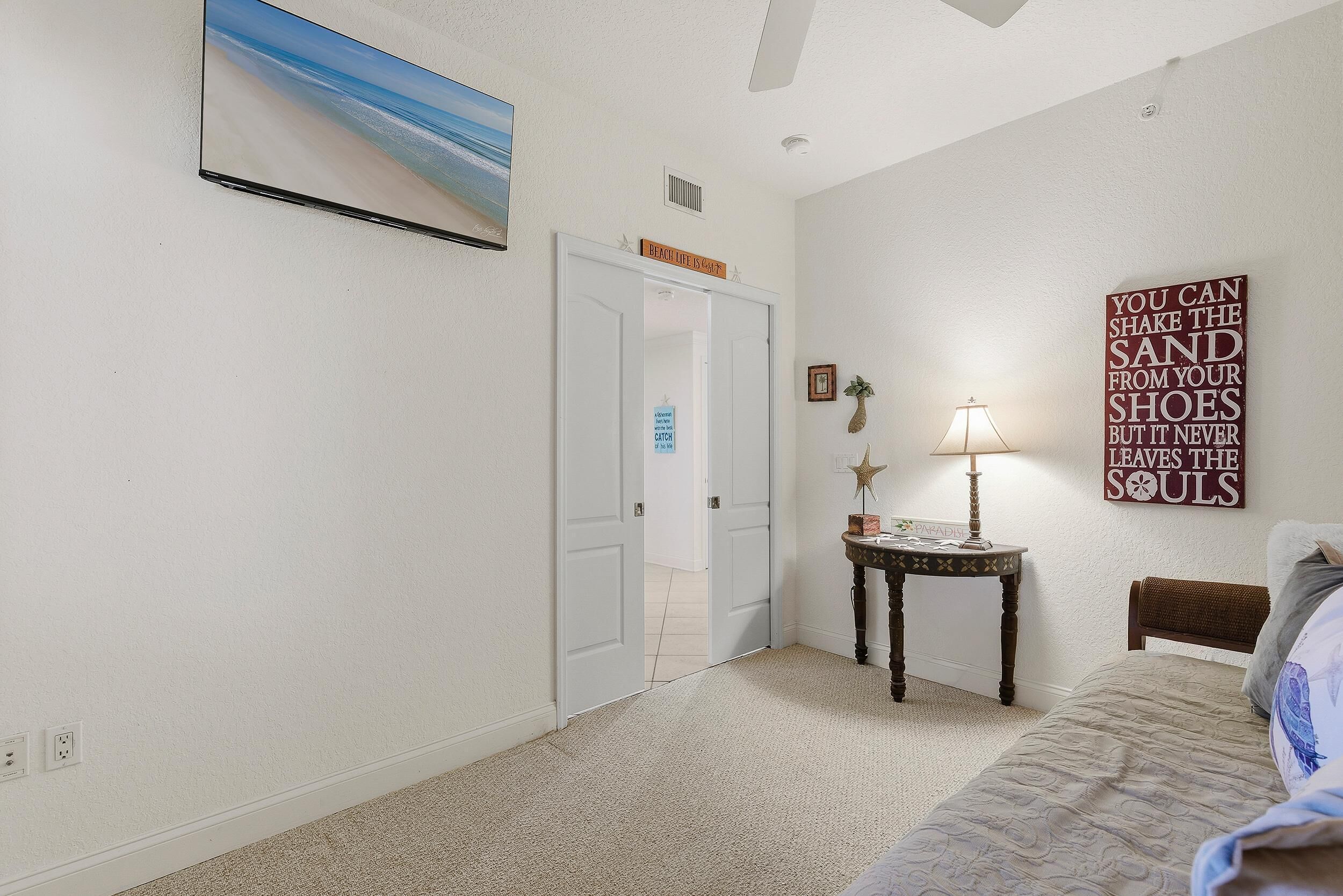 A bedroom with a bed, a nightstand, a lamp, a painting, and a door leading to another room.