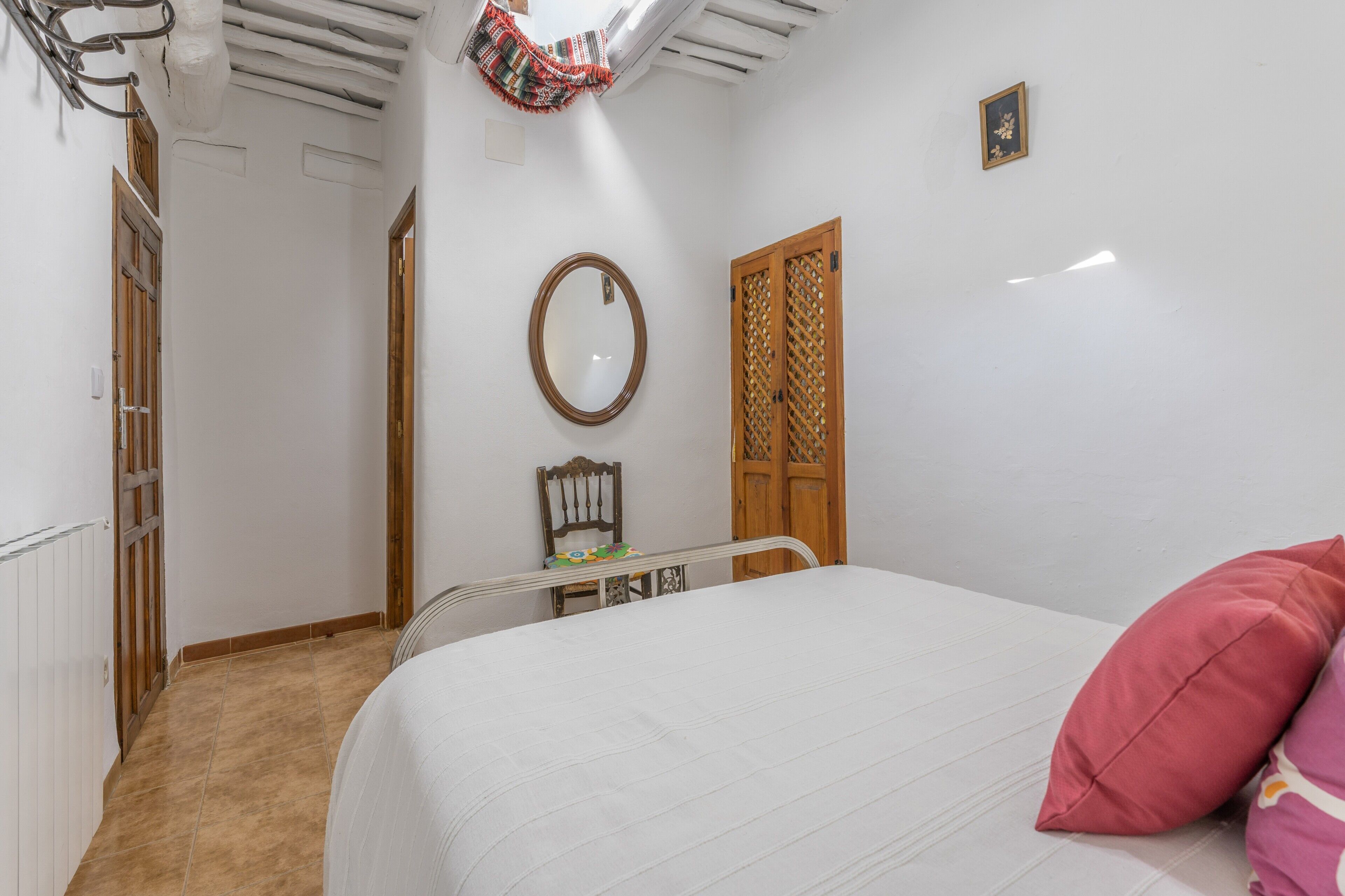 Un dormitorio con cama, puerta de madera, espejo y una silla.
