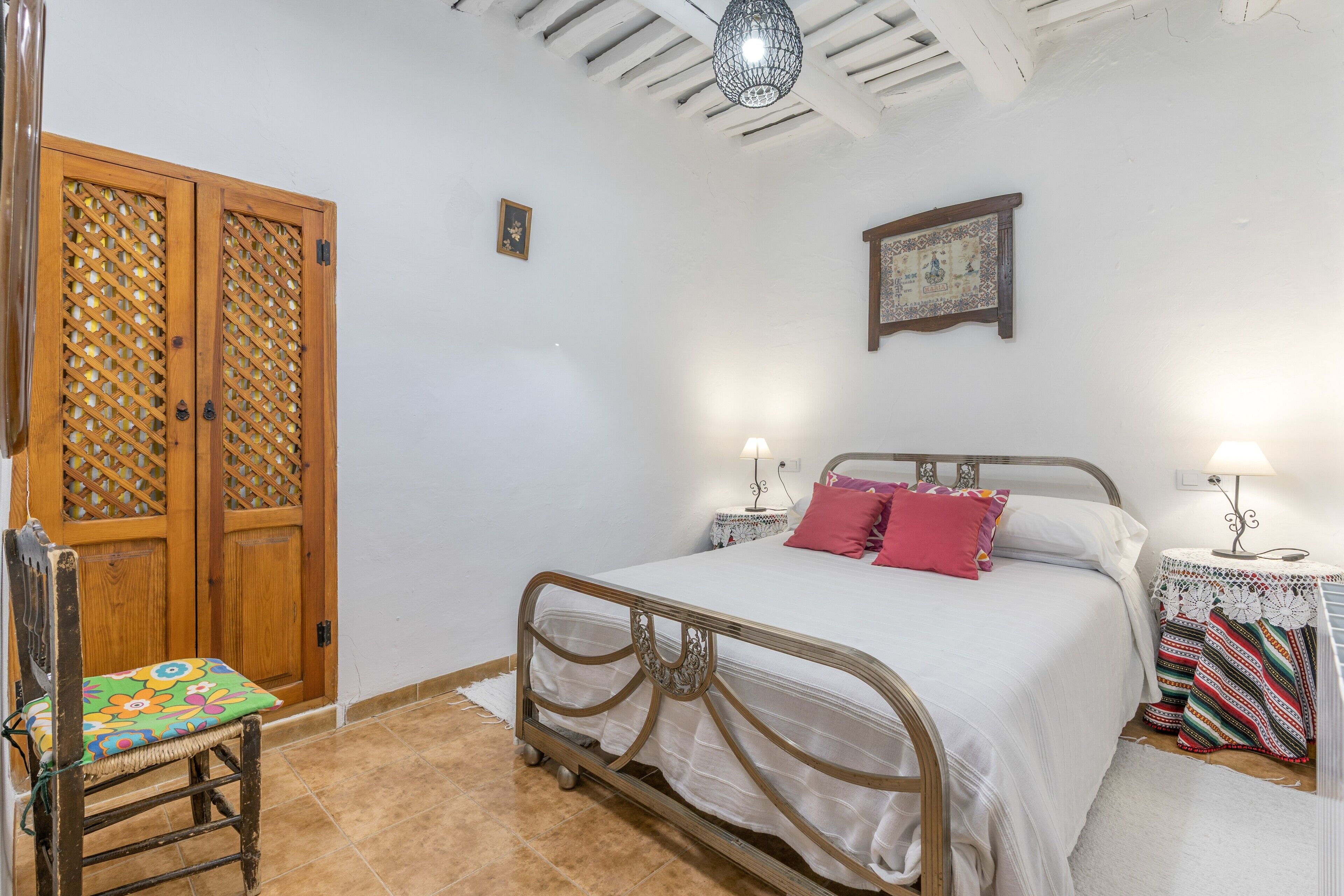 A bedroom with a bed, a chair, a wooden door, and a wall-mounted lamp.