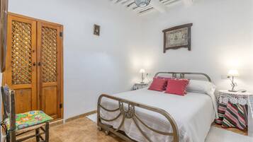A bedroom with a bed, a chair, a wooden door, and a wall-mounted lamp.