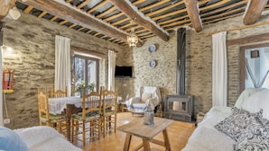Un intérieur rustique avec des murs en pierre apparentes, un plafond en bois, une cheminée, un coin repas avec des chaises et une table, et un canapé.
