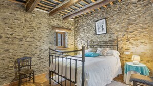 Une chambre aux murs de pierre, avec un lit, une chaise, une petite table et une fenêtre.