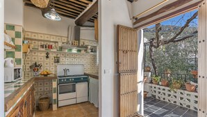 Une cuisine avec un mur recouvert de carreaux, des armoires en bois, une cuisinière et une vue sur l’extérieur grâce à une porte ouverte.