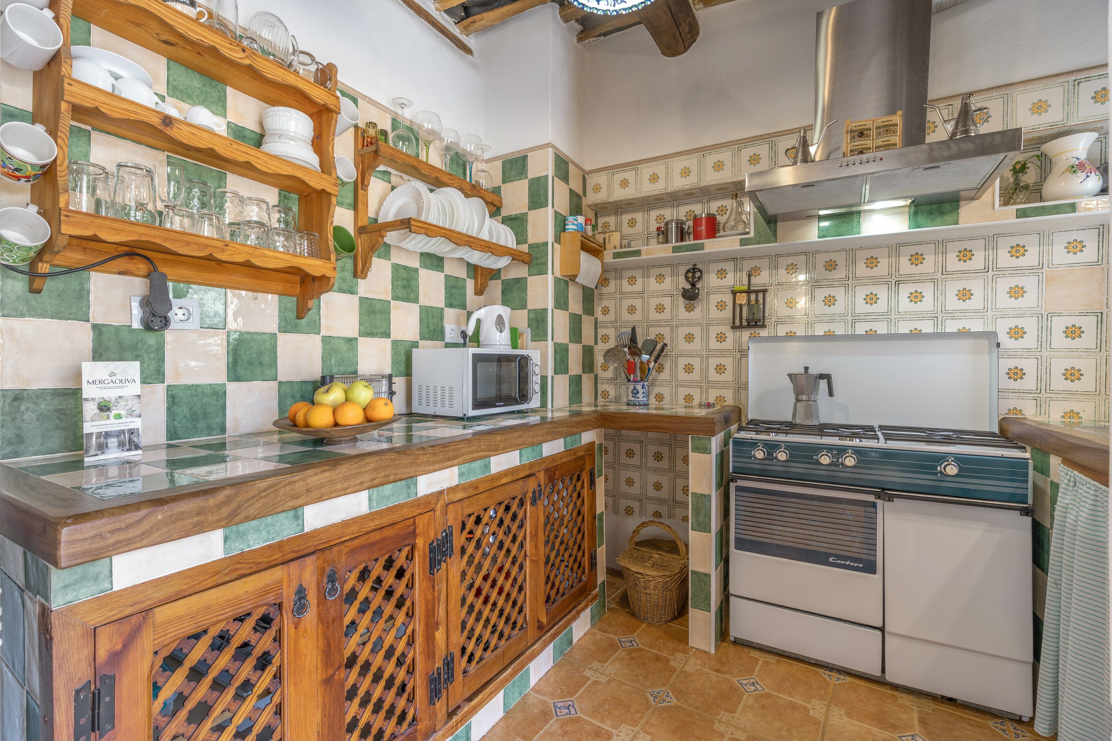 Een keuken met een zwart-wit betegelde spatwand, houten planken met servies, een magnetron en een vintage fornuis.